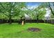 Lush backyard featuring a playset and fire pit, surrounded by mature trees at 1225 N Graham Ave, Indianapolis, IN 46219