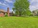 Lush green backyard with a well-maintained lawn, brick house, and mature trees providing ample shade at 1645 Woodview Ln, Anderson, IN 46011