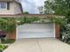 View of a two-car garage adorned with climbing plants and a tidy exterior surrounded by lush greenery at 3232 St Jude Dr, Indianapolis, IN 46227