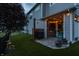 Dusk view of backyard with turf, brick fireplace, string lights, grill, and modern furniture at 7218 Antiquity Dr, Carmel, IN 46033