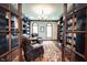 A view through French doors into a handsome library with custom bookshelves and two leather armchairs at 7626 Timber Springs S Dr, Fishers, IN 46038