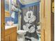 Compact bathroom with blue walls, wooden vanity, toilet, and a Mickey Mouse themed shower curtain at 907 S Ohio St, Sheridan, IN 46069