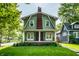 View of home featuring green clapboard siding, brick chimney, covered front porch, and manicured lawn at 357 N Kenyon St, Indianapolis, IN 46219
