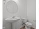 Neutral powder room with round mirror, pedestal sink, toilet, and wood look flooring at 10126 Redwood Peak Ln, Indianapolis, IN 46259