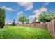 Green backyard features a wood fence, vibrant green grass, mature trees, and a clear blue sky with puffy white clouds above at 14030 Avalon East Dr, Fishers, IN 46037