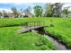 Picturesque backyard features a bridge over a creek with a lush green lawn and surrounding mature trees at 3975 Denwood Dr, Indianapolis, IN 46226