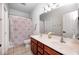 Well-lit bathroom featuring a shower with colorful curtain, tile floors, and a wooden vanity with double sinks at 16285 Remington Dr, Fishers, IN 46037