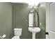 A quaint powder room with a pedestal sink, decorative mirror, and olive-colored walls at 3996 Brockton Manor N Dr, Greenwood, IN 46143