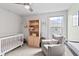 A bedroom with white crib, bookcase, comfortable chair, and a window looking out to the neighborhood at 4629 Rainwater Ln, Whitestown, IN 46075