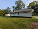 A single-story home shows its vinyl siding, contrasted by lush green grass and a detached garage at 1009 Chestnut St, Anderson, IN 46012