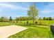 A serene backyard featuring a concrete patio, lush green grass, and open field views with mature trees at 9823 Pica Dr, Fishers, IN 46040
