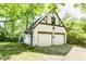 View of a two-car garage with white siding and a charming, Tudor-style design, surrounded by lush greenery and a well-kept lawn at 4302 Kessler Blvd N Dr, Indianapolis, IN 46220
