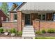 Inviting brick home showcasing a covered porch, decorative details, manicured bushes, and concrete steps to entry at 5912 Evanston Ave, Indianapolis, IN 46220