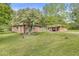 A charming brick house and patio, surrounded by green grass and mature trees under a blue sky at 6401 N Oakland Ave, Indianapolis, IN 46220