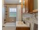 Well-lit bathroom with wood cabinets, sink, bathtub, and patterned shower curtain at 8636 Rockville Rd, Indianapolis, IN 46234