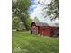 Red outbuilding with a shed roof, featuring a side door and ample storage in a green backyard at 10946 Maze Rd, Indianapolis, IN 46259