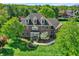 Aerial front view of a grand brick home surrounded by lush greenery, a well-manicured lawn, and mature trees at 13827 Driftwood Dr, Carmel, IN 46033