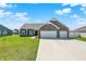 Beautiful single-story home with gray siding, stone details, and a spacious driveway under a blue sky at 49 Manchester Dr, Trafalgar, IN 46181