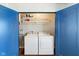 Functional laundry room with a washer, dryer, storage shelves, and bright blue doors at 253 E Minnesota St, Indianapolis, IN 46225