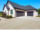Attached three-car garage with black doors and concrete driveway, surrounded by lush landscaping and brick exterior at 8112 Joni Ave, Martinsville, IN 46151