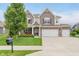 Charming two-story home featuring a brick facade, three-car garage, manicured lawn, and lush landscaping at 15143 Gallop Ln, Fishers, IN 46040