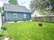 A view of the backyard with a blue house, green grass, and wooden fence at 310 S Butler Ave, Indianapolis, IN 46219