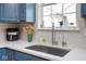 Close up of a kitchen sink, with stainless steel appliances, white countertops, and blue cabinets at 5047 Skipping Stone Dr, Indianapolis, IN 46237