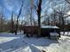 Backyard covered in snow features a small structure with a snow-covered roof, and bare trees against a partly cloudy sky at 8803 S Sleepy Hollow Rd, Waldron, IN 46182