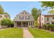 Inviting two-story home showcasing a covered porch, well-manicured lawn, and mature trees under a bright sky at 3614 Guilford Ave, Indianapolis, IN 46205
