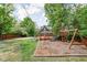Wide shot of the backyard featuring a playground, garden, green grass, wooden fence, and a detached garage at 31 N Bolton Ave, Indianapolis, IN 46219