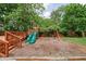 Backyard featuring a wooden playground with slides and swings, set on a mulch bed, surrounded by mature trees at 31 N Bolton Ave, Indianapolis, IN 46219