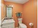 Cozy bathroom with a pedestal sink, toilet, and bright orange walls at 9054 Cinnebar Dr, Indianapolis, IN 46268