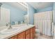 Bathroom with double vanity, wood cabinets, mirror, and shower with curtain at 9311 Windrift Way, Zionsville, IN 46077