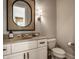 Stylish powder room with a rattan-framed mirror, decorative sconce, and a white vanity at 7601 W Stonegate Dr, Zionsville, IN 46077