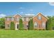 Beautiful brick home with manicured lawn, symmetrical evergreens and classic architectural details, under a clear blue sky at 3267 Cimmaron Ash Ct, Zionsville, IN 46077