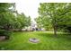 Large, grassy backyard with mature trees, a fire pit, and a partial view of the house, ideal for outdoor living at 9127 Pointe Ct, Fishers, IN 46037