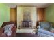 Living room with a brick fireplace, chairs, and wood paneling in need of some TLC at 2840 W 12Th St, Anderson, IN 46011