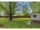 Large backyard featuring a storage shed, wooden fence, green grass, large tree, and puddle at 8218 San Carlos Ct, Indianapolis, IN 46256