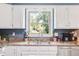Close-up of a kitchen sink with granite countertops, white cabinets, and a view of the backyard at 9832 Scotch Pine Ln, Indianapolis, IN 46256