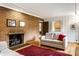 Cozy living room featuring a brick fireplace, red rug, and view into the kitchen at 100 Wellington Rd, Indianapolis, IN 46260