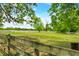Expansive green pasture enclosed by a wooden fence, framed by mature trees and a clear blue sky at 5335 W 550 S, Trafalgar, IN 46181