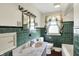 Vintage bathroom featuring green tile walls, a classic vanity, and a window adorned with decorative curtains at 10036 E Troy Ave, Indianapolis, IN 46239