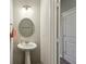 Small powder room featuring neutral paint, round mirror, pedestal sink, hand towel, and open door at 1270 Shaw Ln, Shelbyville, IN 46176