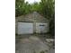 Exterior view of a two-car garage with peeling paint and overgrown foliage at 1168 N Gladstone Ave, Indianapolis, IN 46201
