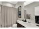 Well-lit bathroom featuring a shower with gray curtains, white sink and vanity, and decorative wall art at 1334 Sunnybrook Ln, Greenwood, IN 46143
