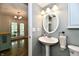 Cozy half-bathroom features pedestal sink and decorative oval mirror, with a glimpse of the sunroom at 16857 Palmetto Way, Noblesville, IN 46062