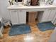 Bright bathroom with double sinks, white cabinetry, neutral walls, and wood look flooring with blue rugs at 4962 Potomac Square Pl, Indianapolis, IN 46268