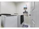 Bright laundry room with white washer and dryer, a shelf with supplies, and a set of hangers at 6822 Woodford Ln, Indianapolis, IN 46237