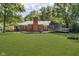 Expansive backyard featuring lush green grass, a brick home, mature trees, and an outdoor fireplace at 7734 Hoover Rd, Indianapolis, IN 46260