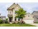 Charming two-story home with tan siding, stone accents, a well-manicured lawn, and lush landscaping at 7824 Hedgehop Dr, Zionsville, IN 46077